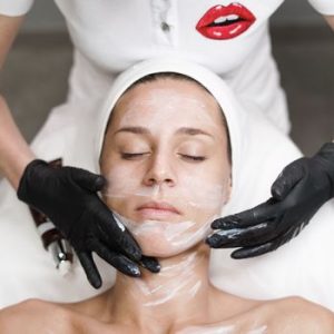 Woman receiving a facial treatment at spa, with beautician applying mask in a relaxing setting.