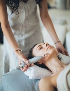 A woman enjoying a relaxing facial treatment using advanced technology at a spa. Perfect for wellness promotion.