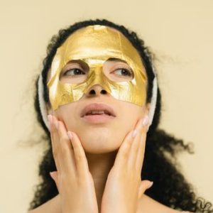 Close-up of woman wearing a gold sheet mask for skincare in a studio setting.